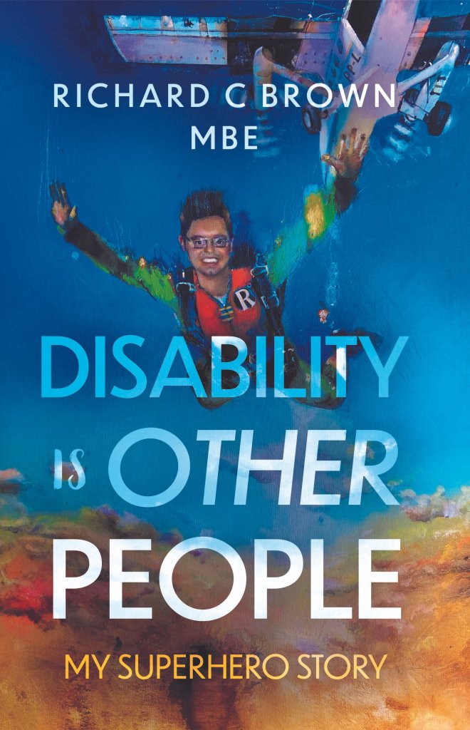 Book cover. Richard is wearing a Robin costume and skydives in a deep blue sky over golden clouds from a plane. He is smiling.